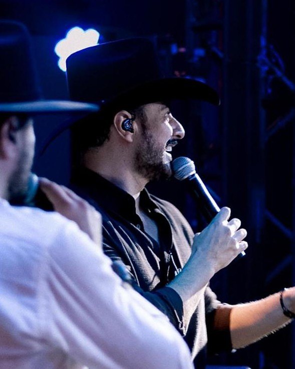 Cantor de chapéu ao microfone, sob luz azul de palco
